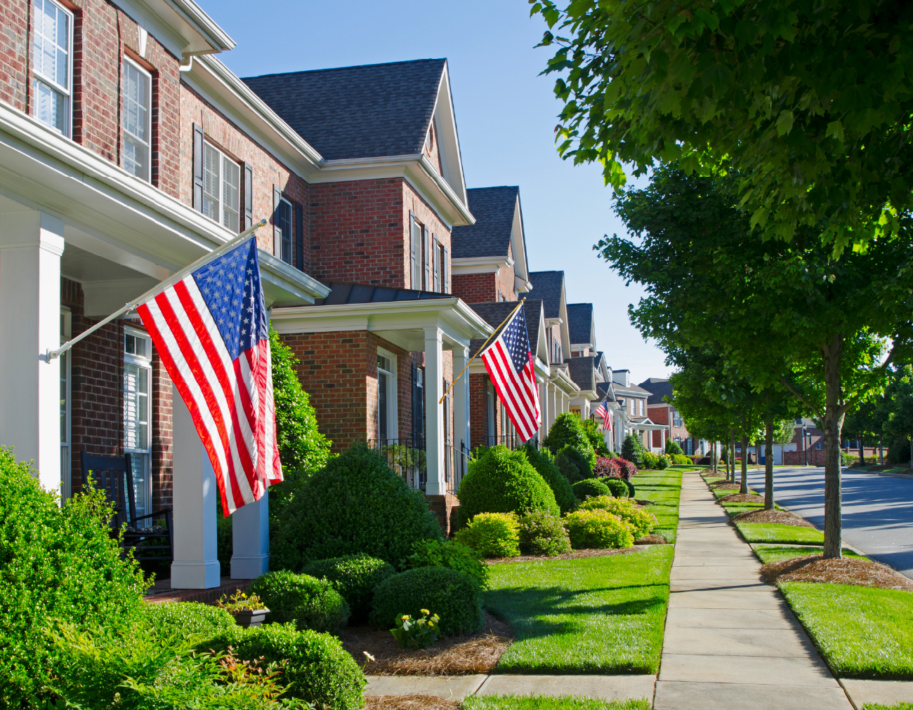 Tree-lined residential street with American flags displayed outside homes